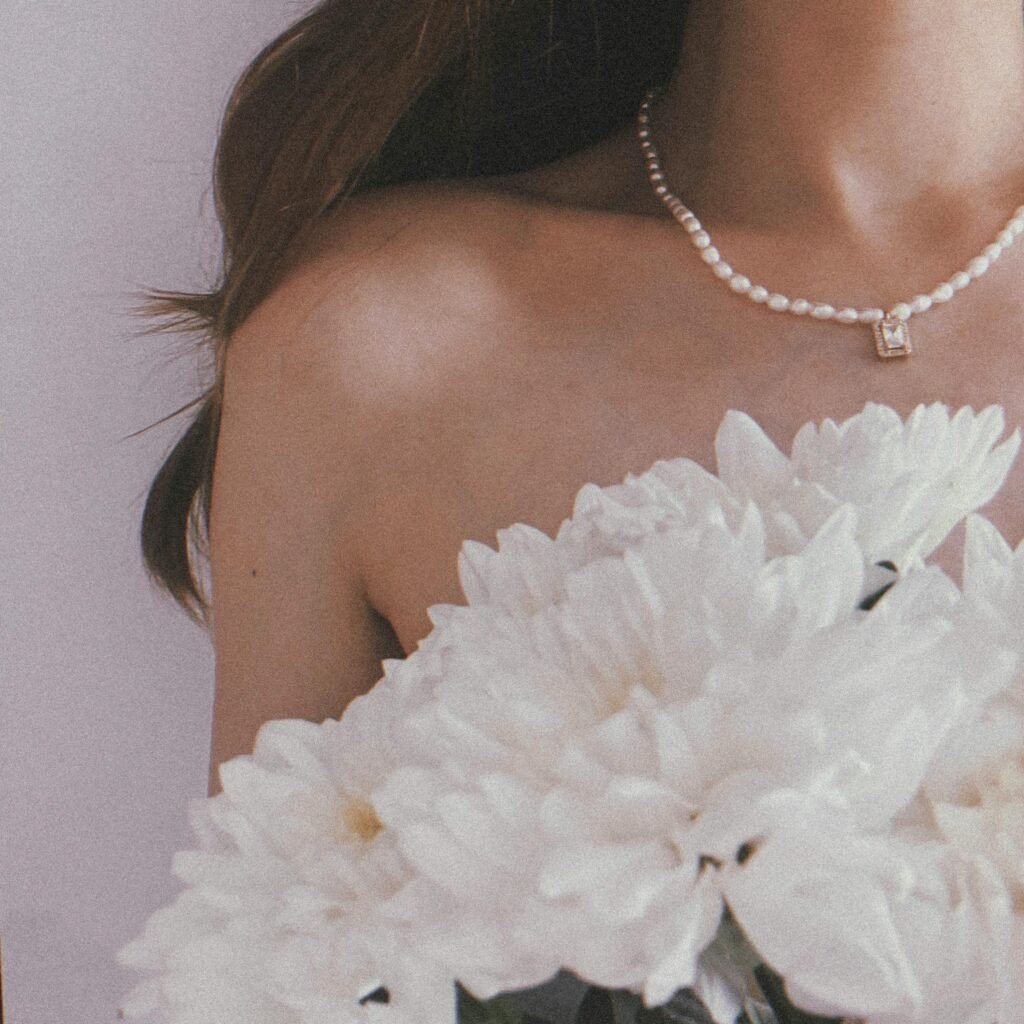 A woman in a pearl necklace holding white flowers, symbolizing elegance and purity.