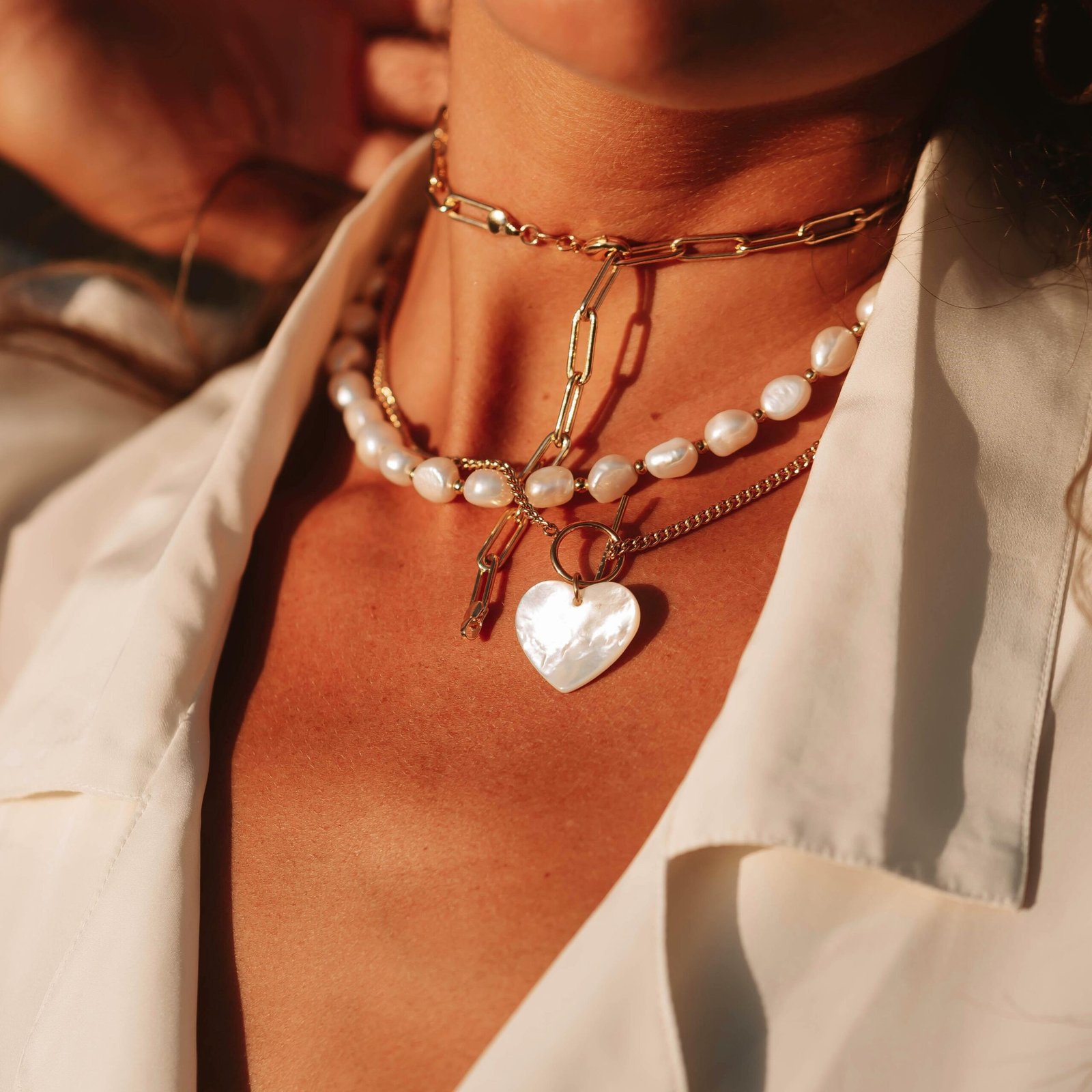 Close-up of elegant layered necklaces featuring pearls and gold chains on sunlit skin.